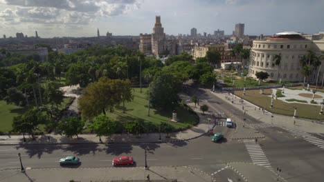 Old-classic-American-cars-turning-on-street-next-to-capitol,-in-Havana,-Cuba