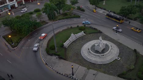 high-angle-establishing-shot-of-classic-cars-turning-on-street-roundabout-in-Havana,-Cuba-in-evening