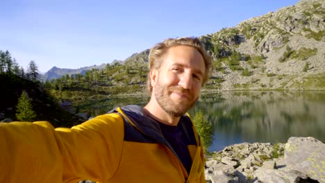 Young-man-taking-selfie-at-mountain-lake.-Man-hiking-in-Switzerland-takes-selfies-surrounded-by-stunning-mountain-landscape.-Selfie-travel-adventure-lifestyle