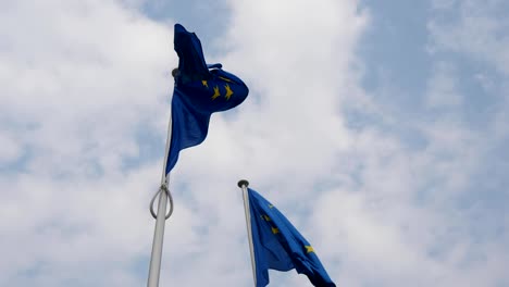 Maravillosa-vista-de-dos-banderas-de-la-Unión-Europea-ondeando-en-la-sede-de-la-UE-en-Bruselas-en-un-día-soleado-en-primavera.-El-cielo-es-celeste-y-blanco.