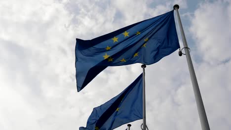 Splendid-view-of-two-European-Union-flags-waving-solemnly-in-Brussels-on-a-sunny-day-in-spring-in-slo-mo-The-sky-is-blue-and-white