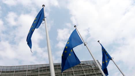 Beeindruckende-Aussicht-auf-drei-Flaggen-der-Europäischen-Union,-die-an-einem-sonnigen-Frühlingstag-am-EU-Hauptsitz-in-Brüssel-flattern.-Der-Himmel-ist-blau-und-weiß.