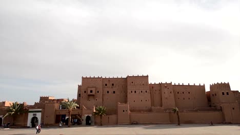 People-walking-and-cars-passing-by-in-front-of-the-outer-walls-of-the-front-façade-of-Kasbah-Taourirt