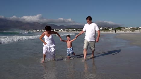 Slow-motion-of-couple-swinging-child-through-waves,-South-Africa