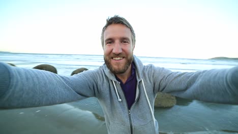 Cheerful-man-stands-near-the-Moeraki-boulders,takes-selfie-portrait