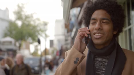 Young-Man-Using-Phone-As-He-Walks-Along-Busy-City-Street