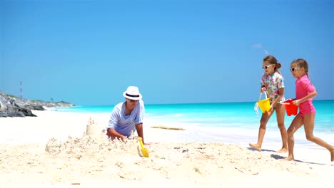 Young-father-and-little-kids-making-sand-castle-at-tropical-beach