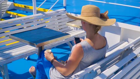 Young-beautiful-woman-texting-on-smartphone-sitting-on-seat,-summer-beach-clothes