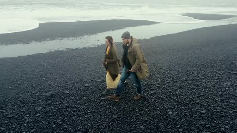 Aerial-view-of-the-young-hipster-couple-walking-on-black-volcanic-beach-in-Iceland.-Man-and-woman-enjoying-the-nature