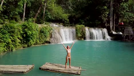 Drohne-Schuss-junge-Frau-auf-Bambus-Floß-umarmen-Natur-am-Wasserfall-im-Regenwald,-Arme-weit-öffnen-Menschen-reisen-Urlaub-Konzept.-4K-Auflösung,-Philippinen