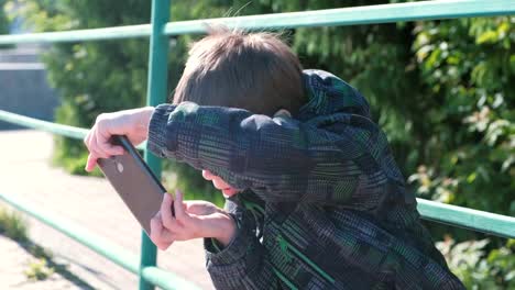 El-niño-juega-un-juego-en-su-teléfono-móvil-mientras-está-sentado-en-el-parque.