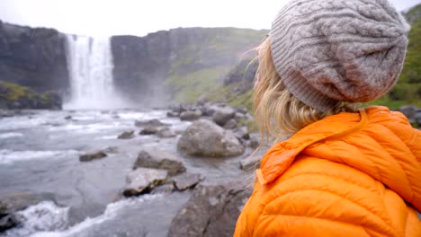 Junge-Frau-in-Island-machen-Herz-Formrahmen-Finger-auf-spektakulären-Wasserfall