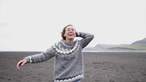 Junge-Frau-ausgestreckten-durch-das-Meer-stehend-am-schwarzen-Sandstrand,-Haare-im-Wind-Island---weiblich-verspielt-genießen-Natur-und-Freiheit---Slow-Motion-läuft