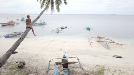 Drone-point-of-view-of-young-woman-on-palm-tree-contemplating-paradise