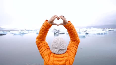 Mujer-joven-haciendo-marco-del-dedo-corazón-forma-en-Laguna-glaciar-en-Islandia