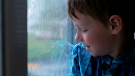 Boy-looks-out-the-window-in-the-rain-and-is-sad.