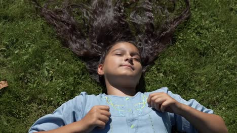 Chica-joven-con-largo-cabello-negro-se-encuentra-en-la-espalda-en-el-parque-en-tiempo-soleado.-4K