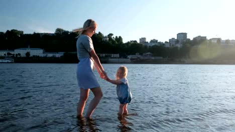 Mutter-und-Mädchen-spielen-am-Strand-des-Flusses-bei-Sonnenuntergang-und-Schwimmen.