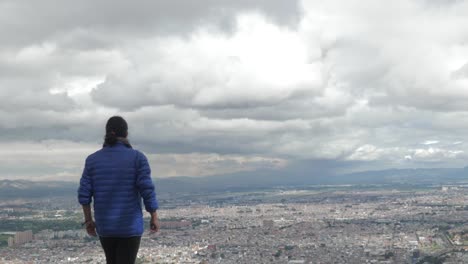 Mujer-caminando-hacia-y-mirando-a-la-ciudad-de-Bogotá-desde-las-montañas,-en-cámara-lenta