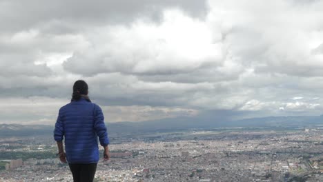 Woman-walking-towards-and-looking-at-the-city-of-Bogota-from-the-mountains,-in-slow-motion