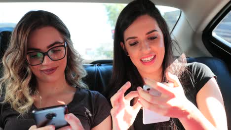 Candid-friends-holding-cellphones-in-the-back-seat-of-a-taxi-typing-and-sending-messages.-Girlfriends-browsing-the-internet