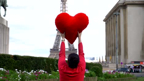 Mujer-joven-girando-alrededor-frente-a-torre-de-Eiffel-con-corazón-rojo-en-sus-manos-en-cámara-lenta-180-fps