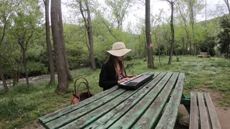 junge-und-schöne-Frau-spielen-Synthesizer-auf-dem-Tisch-eines-Parks,-Frankreich