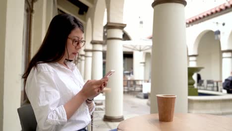 Frau-im-sitzen-und-SMS-auf-Handy-im-café