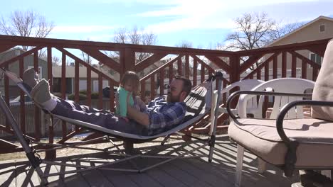 Dad-playing-with-toddler-on-outdoor-deck-hammock-in-summer-sun.