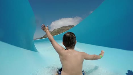 Happy-young-boy-going-down-curved-waterslide-in-slow-motion