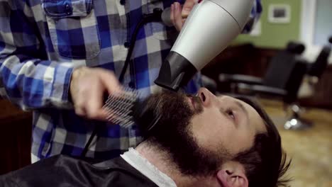 Barbero-del-secado-de-barba-de-un-hombre-barbudo-con-secador-de-pelo-en-una-barbería