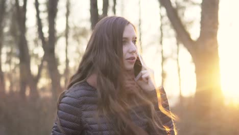 Young-attractive-woman-emotionally-talking-on-the-phone-for-a-walk-in-the-park-at-sunset