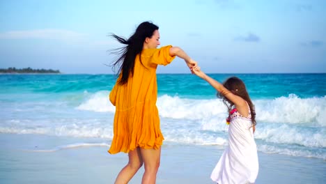 Niña-adorable-y-joven-madre-en-playa-tropical-cálida-noche-con-hermosa-puesta-de-sol