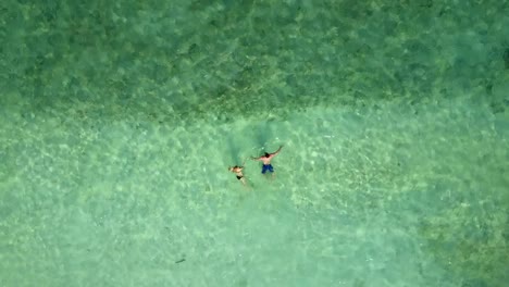 Par-de-nadar-en-el-Océano-Índico-en-una-playa-vacía,-ver-desde-arriba.-Imágenes-aéreas-de-dos-amantes-en-luna-de-miel-en-mar-azul-Esmeraldo