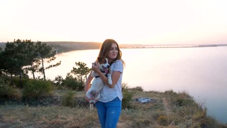 Mujer-atractiva-joven-jugando-con-un-perro-Jack-Russell-en-el-Prado-al-atardecer-con-el-fondo-del-mar.-cámara-lenta