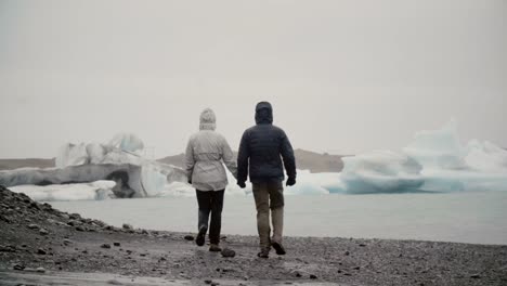 Rückansicht-des-jungen-Paares-gehen-in-Eis-Lagune-in-Island.-Mann-und-Frau-die-Eisberge-und-Gletscher-erkunden