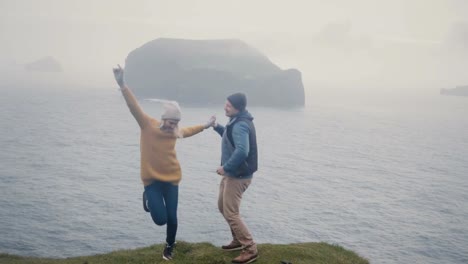 Young-stylish-couple-having-fun-together.-Man-and-woman-dancing-on-the-shore-of-the-sea-in-foggy-day