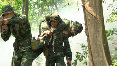 Soldier-holding-gun-weapon-and-waring-armor-uniform-with-smoke.-Soldiers-are-taking-the-wounded-man-out-of-the-jungle.