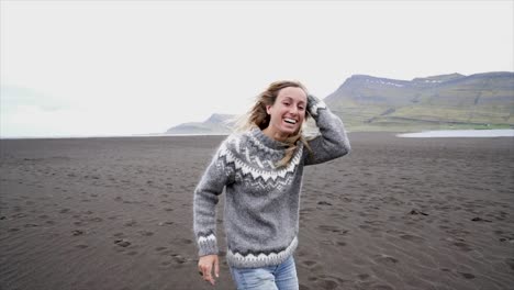 Young-woman-arms-outstretched-by-the-sea-standing-on-black-sand-beach,-hair-in-wind--Iceland---Female-running-playful-enjoying-nature-and-freedom--Slow-motion