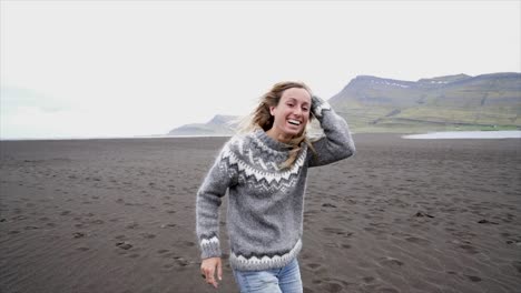 Brazos-de-la-joven-extendidos-por-el-pie-de-mar-en-la-playa-de-arena-negra,-de-pelo-en-el-viento-Islandia---mujer-correr-juguetón-disfrutar-naturaleza-y-libertad---lenta