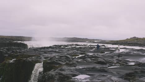 Joven-inconformista-pareja-varada-cerca-de-la-cascada-de-gran-alcance-en-Islandia-y-disfrutando-de-la-vista