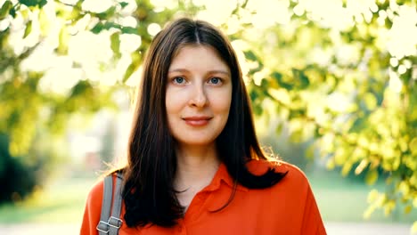 Close-up-Portrait-schöne-Mädchen-mit-braunen-Haaren,-Blick-in-die-Kamera-und-lächelnd-mit-Sommerpark-im-Hintergrund.-Sommer,-Sonnenschein-und-entspannte-Menschen-Konzept.