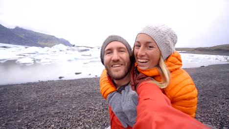 4-K-Video-der-jungen-Paare,-die-Spaß-unter-Selfie-durch-den-Gletschersee-Jökulsárlón-Lagune-in-Island.-Zwei-Personen-Reisen-Liebe-Romantik-Kommunikationskonzept-miteinander-teilen.-Frühling,-Kälte