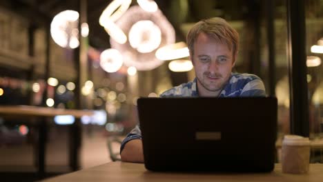 Handsome-businessman-drinking-coffee-while-using-laptop-at-night
