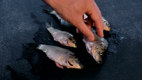 Man-plays-with-fresh-clean-carp-fish-on-black-table.-Cooking-fish.-Close-up-hand.