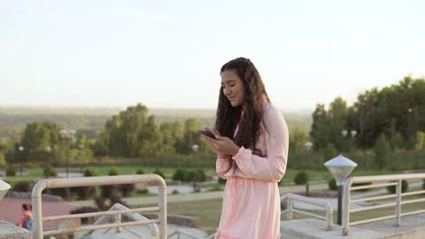 The-girl-walks-in-the-park-near-the-Ferris-wheel-and-uses-a-smartphone.-4K