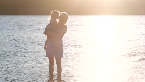 Beautiful-blonde-mother-and-daughter-walk-along-the-river-on-the-water-at-sunset.