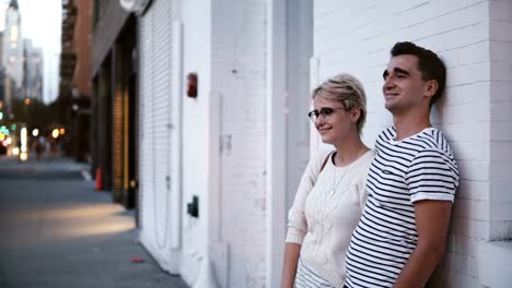 Feliz-joven-pareja-romántica-auténtica-están-parados-juntos-en-una-fecha-por-muro-de-edificio-blanco-en-Soho,-Nueva-York-de-noche