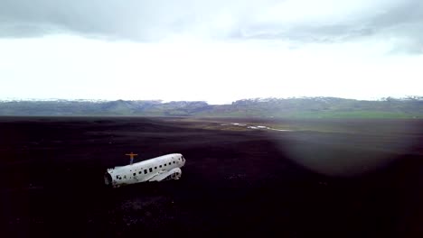 Drone-view-aerial-of-Young-man-stands-arms-outstretched-on-airplane-crashed-on-black-sand-beach-looking-around-her-contemplating-surroundings-Famous-place-to-visit-in-Iceland-and-pose-with-the-wreck--4K-resolution