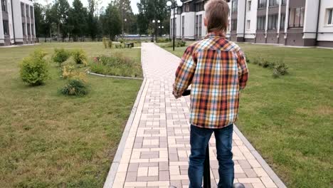 Unrecognizable-boy-is-rolling-on-gyro-scooter-near-the-home.-Back-view.